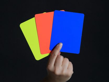 يد تحمل 3 بطاقات صفراء وحمراء وزرقاء - AFP