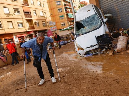 رجل يسير على عكازات قرب سيارة متضرّرة نتيجة فيضانات فالنسيا - 1 نوفمبر 2024 - Reuters