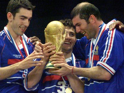 زين الدين زيدان وبيكسينتي ليزارازو يحملان كأس العالم أمام روبير بيريس في باريس - 12 يوليو 1998 - Reuters