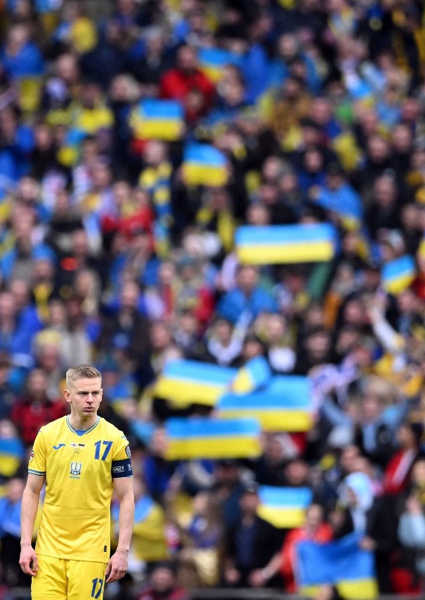 أعلام أوكرانية يرفعها مشجعون وراء قائد منتخب أوكرانيا أولكسندر زينتشينكو خلال المباراة ضد إنجلترا - 26 مارس 2023
